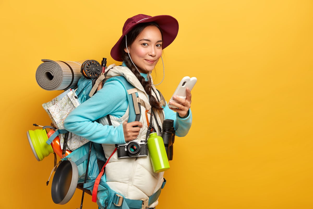 pretty-satisfied-traveler-uses-free-internet-connection-smartphone-blogging-during-wanderlust-trip-carries-big-heavy-rucksack